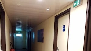 A hotel hallway with wooden flooring, doors on the right, and a fire extinguisher on the left. - Brit Hotel Saint-Quentin (Fayet)