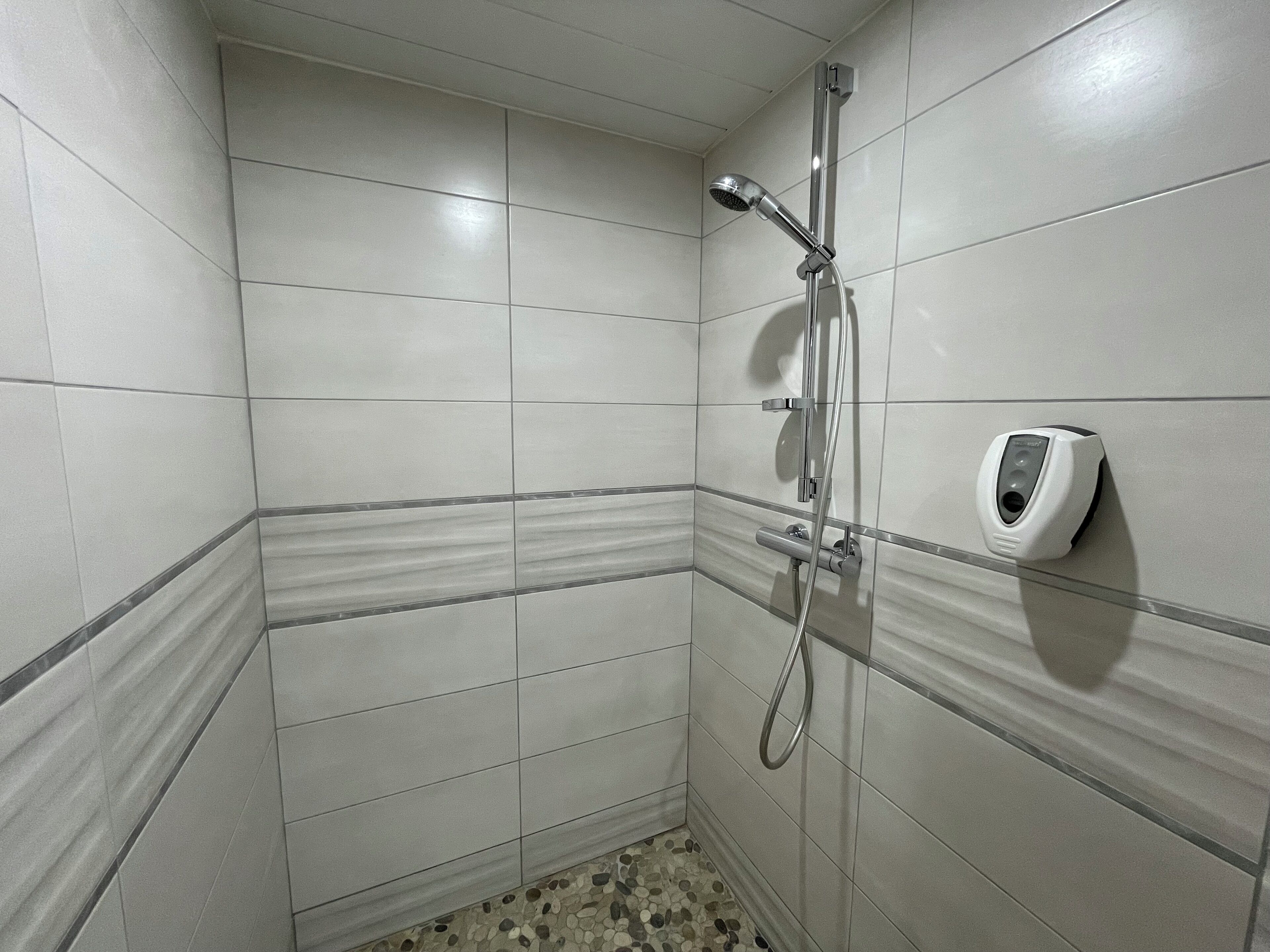 A small, tiled shower area with a handheld showerhead and a wall-mounted soap dispenser.