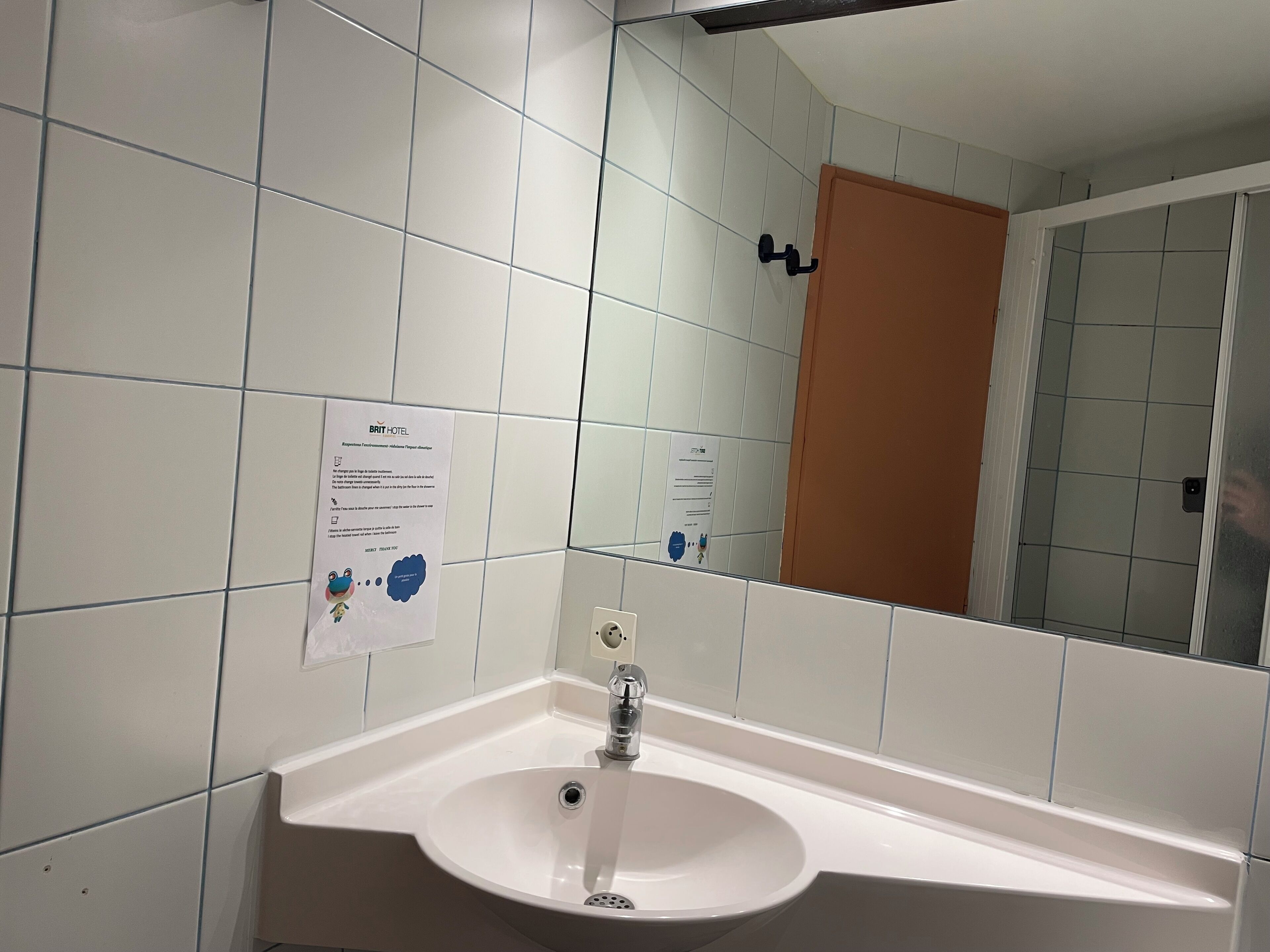Un baño con azulejos blancos, un lavabo, un espejo y una puerta.