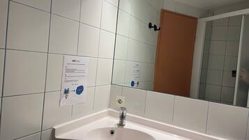 Un baño con azulejos blancos, un lavabo, un espejo y una puerta.