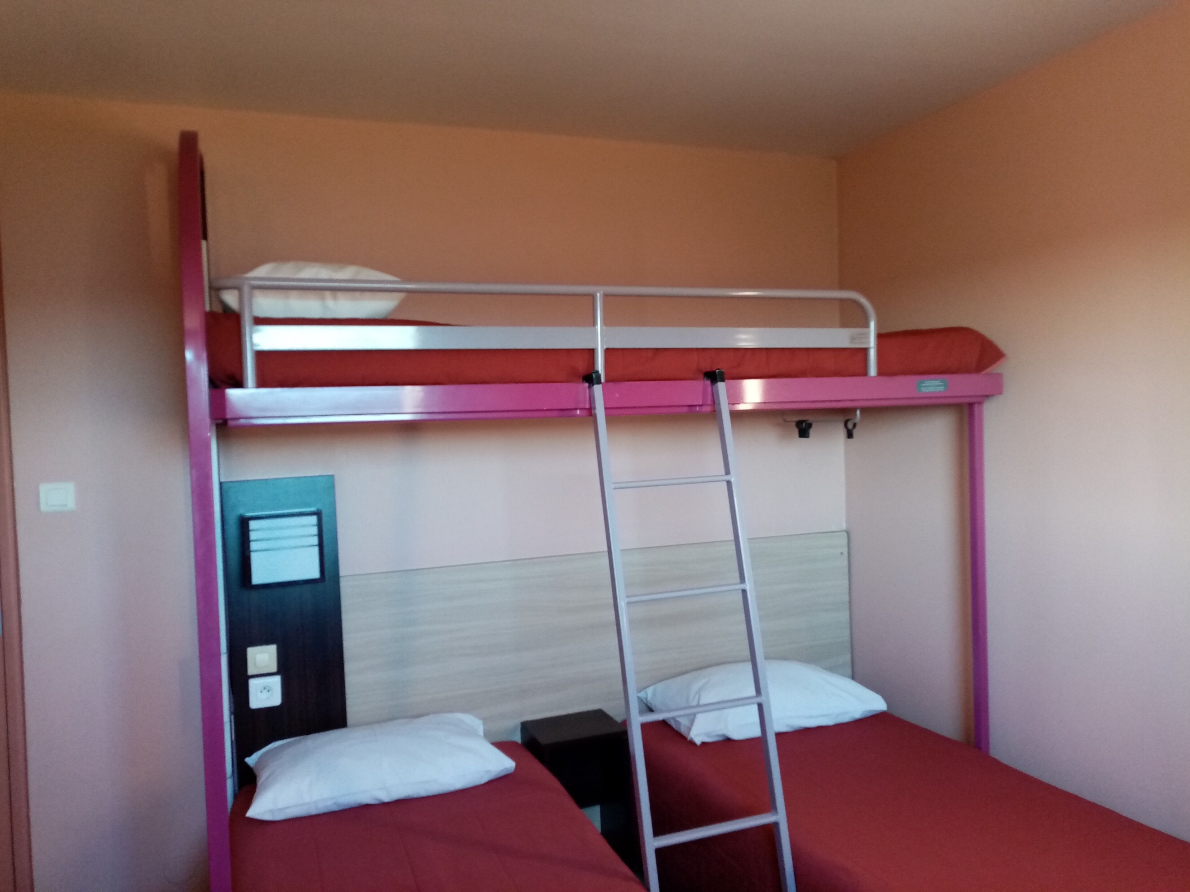 Een stapelbed met een ladder, twee kussens en een houten hoofdbord.