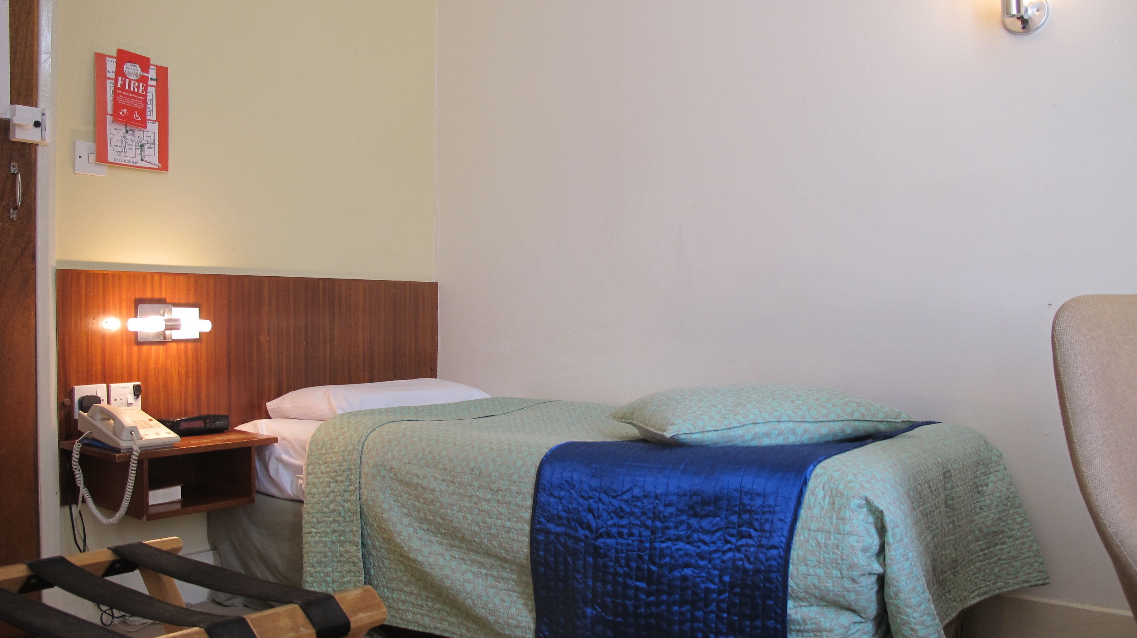 A hotel room with a bed, a bedside table with a telephone, and a wall-mounted light fixture.