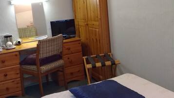 A bedroom with a bed, a desk with a computer, a chair, a wardrobe, and a wall-mounted picture.