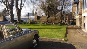Un coche estacionado en una calle con un área verde y un edificio al fondo.