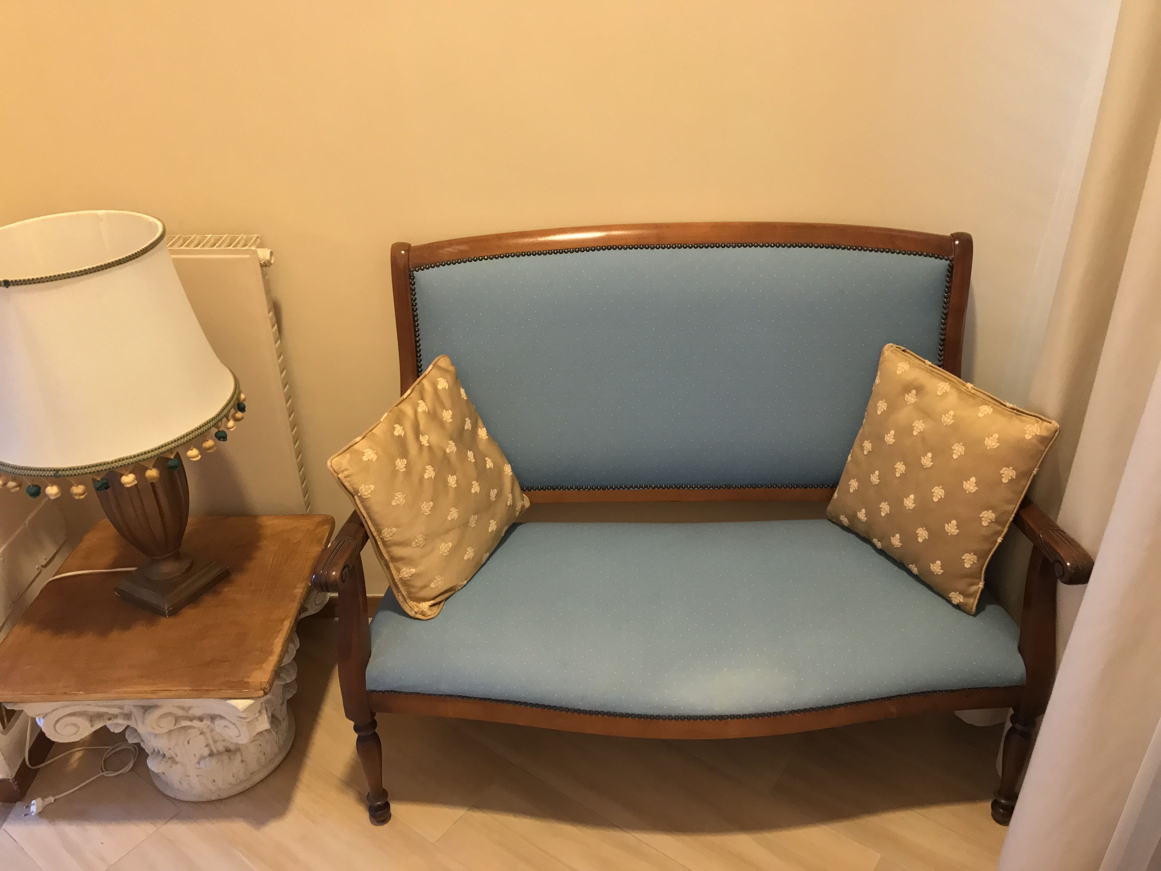 Een blauwe bank met twee gekleurde kussens, een lamp en een bijzettafeltje met een decoratieve voet.