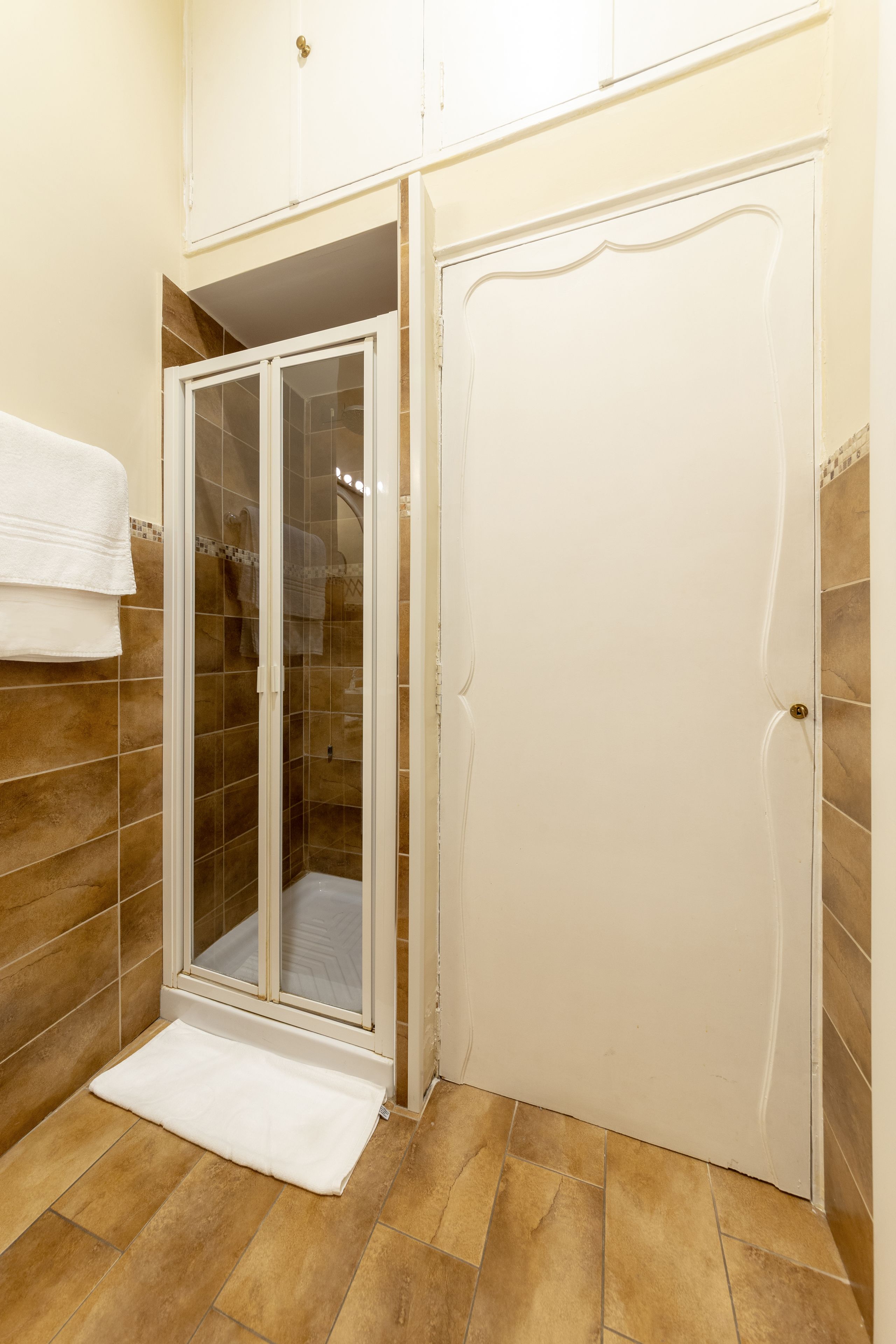 A bathroom with a glass-enclosed shower, a white door, and a white towel on the floor.