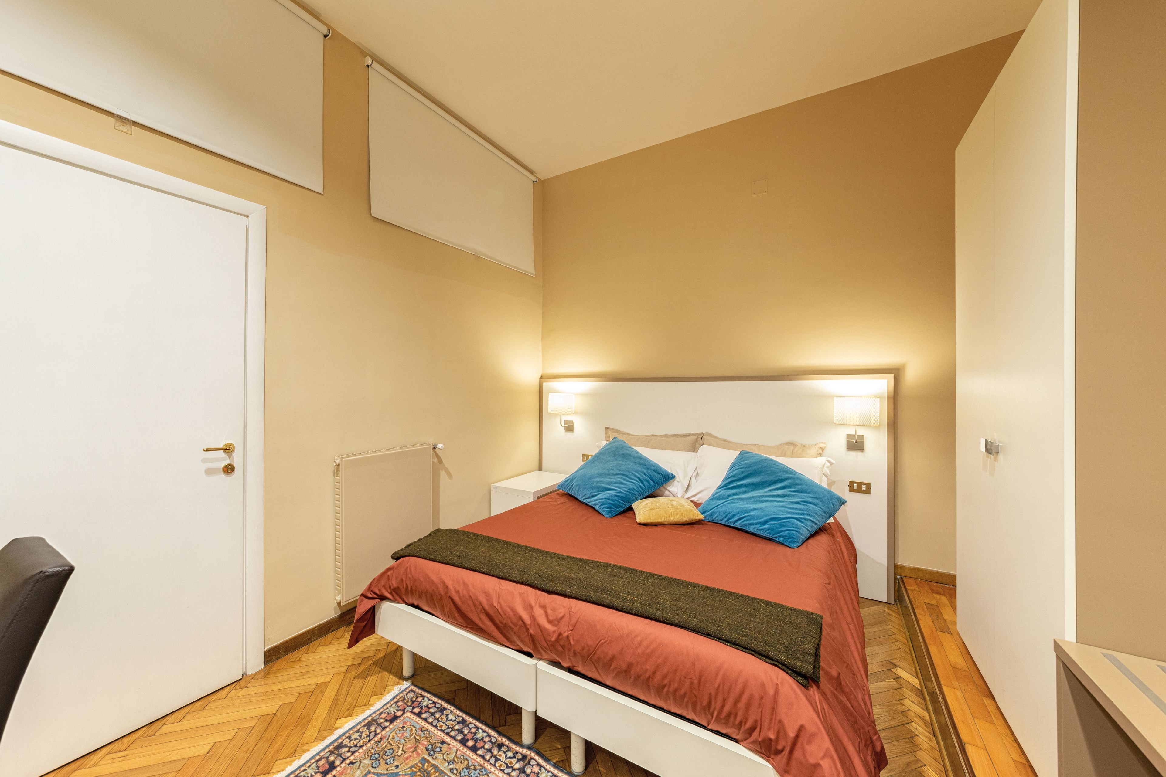 A bedroom with a bed, bedside tables, a chair, a radiator, and a door.