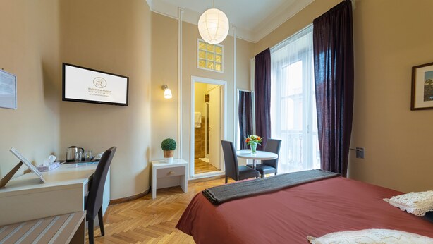 Habitación de hotel con cama, escritorio con laptop, silla, mesita con un florero y ventana con cortinas.