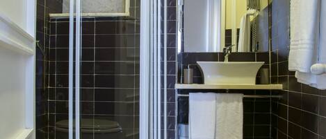A bathroom with a glass-enclosed shower, a white toilet, a sink with a mirror, and a towel rack.