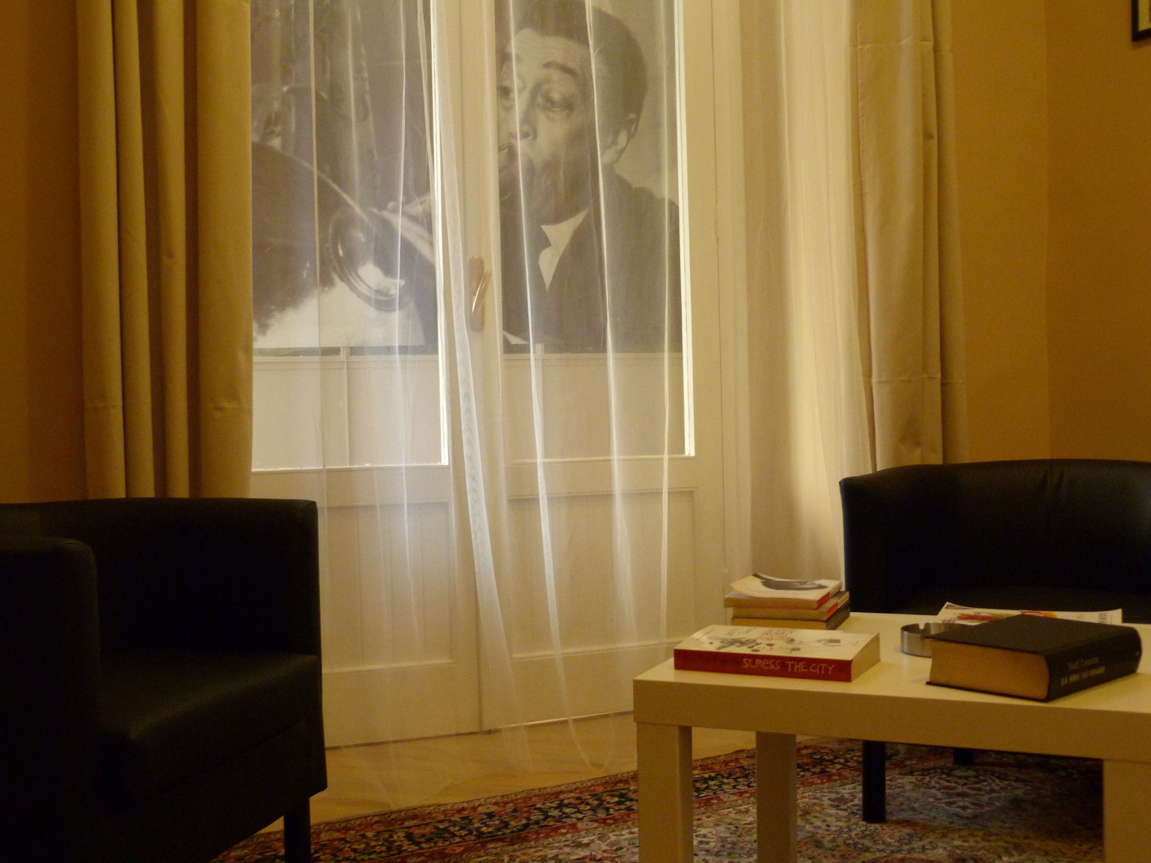A room with a large window, a table with books, and two chairs.