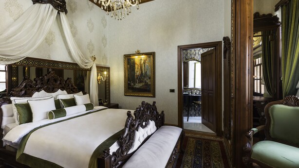 A large, ornate bed with a canopy, a chandelier, and a painting on the wall. - Hotel 1207 Special Class (Antalya)
