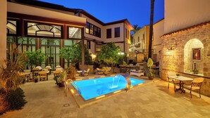 A poolside area with outdoor seating, a swimming pool, and a stone wall with a mural. - Hotel 1207 Special Class (Antalya)