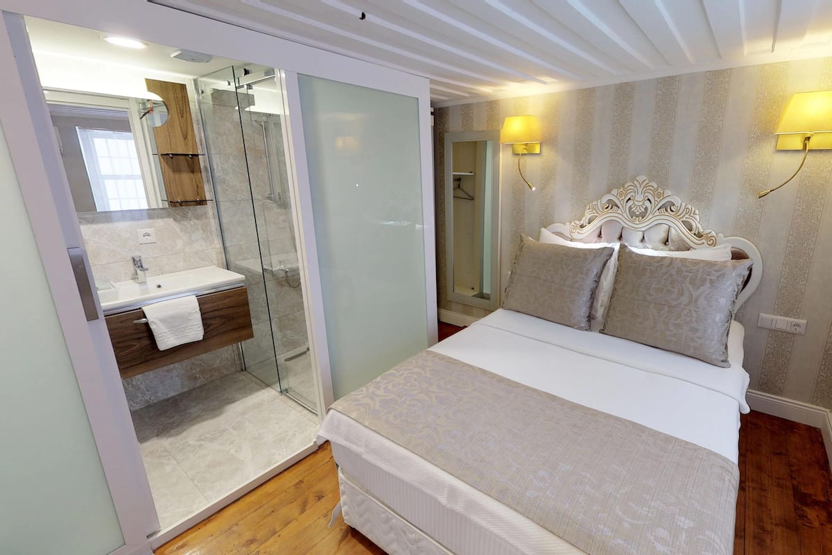 Een slaapkamer met een bed, een badkamer met een douchecabine van glas, en twee wandlampen.