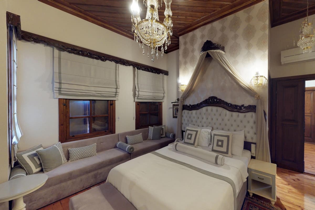 Een slaapkamer met een groot bed, een bankje, een kroonluchter en een houten plafond.
