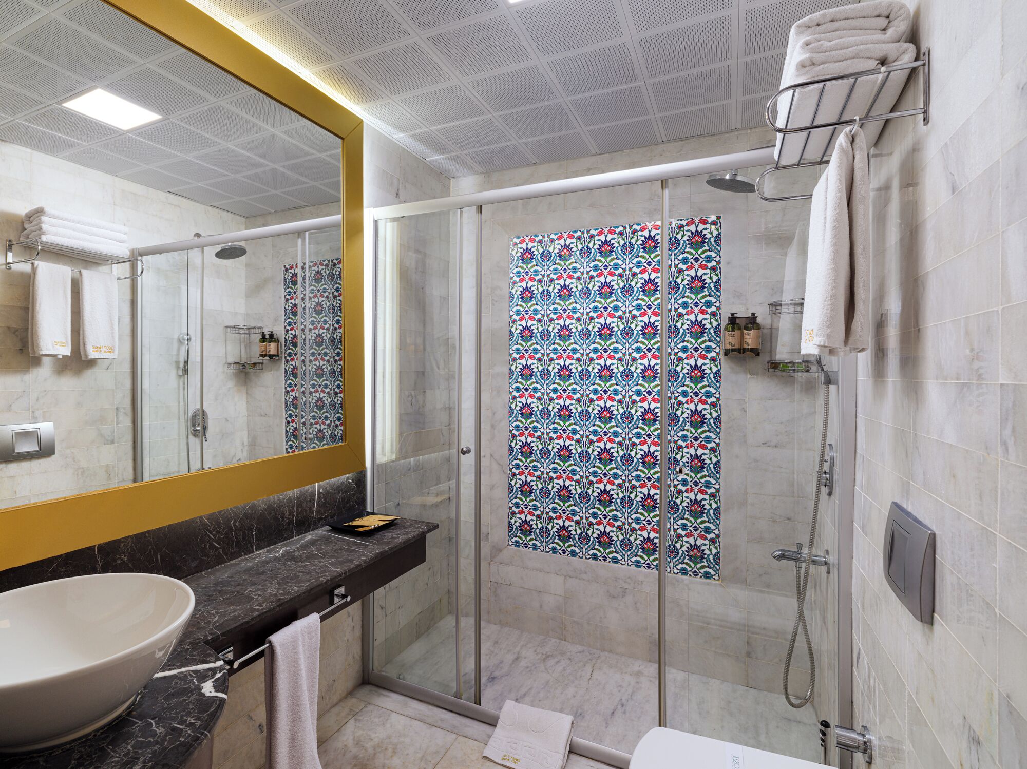 A modern bathroom with a large mirror, a glass shower enclosure, and a marble countertop.
