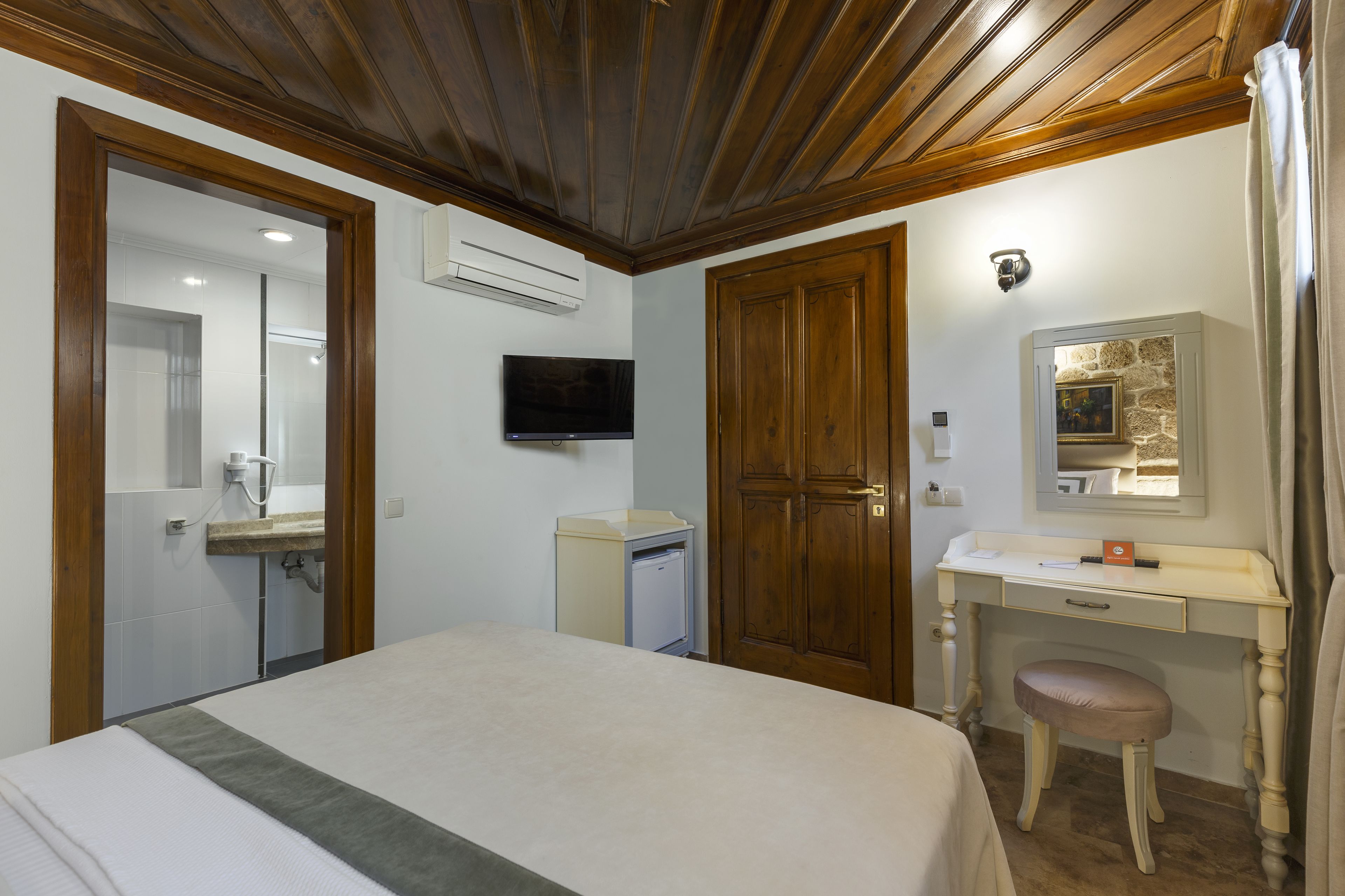 A bedroom with a bed, a desk with a chair, a television, and a wardrobe.