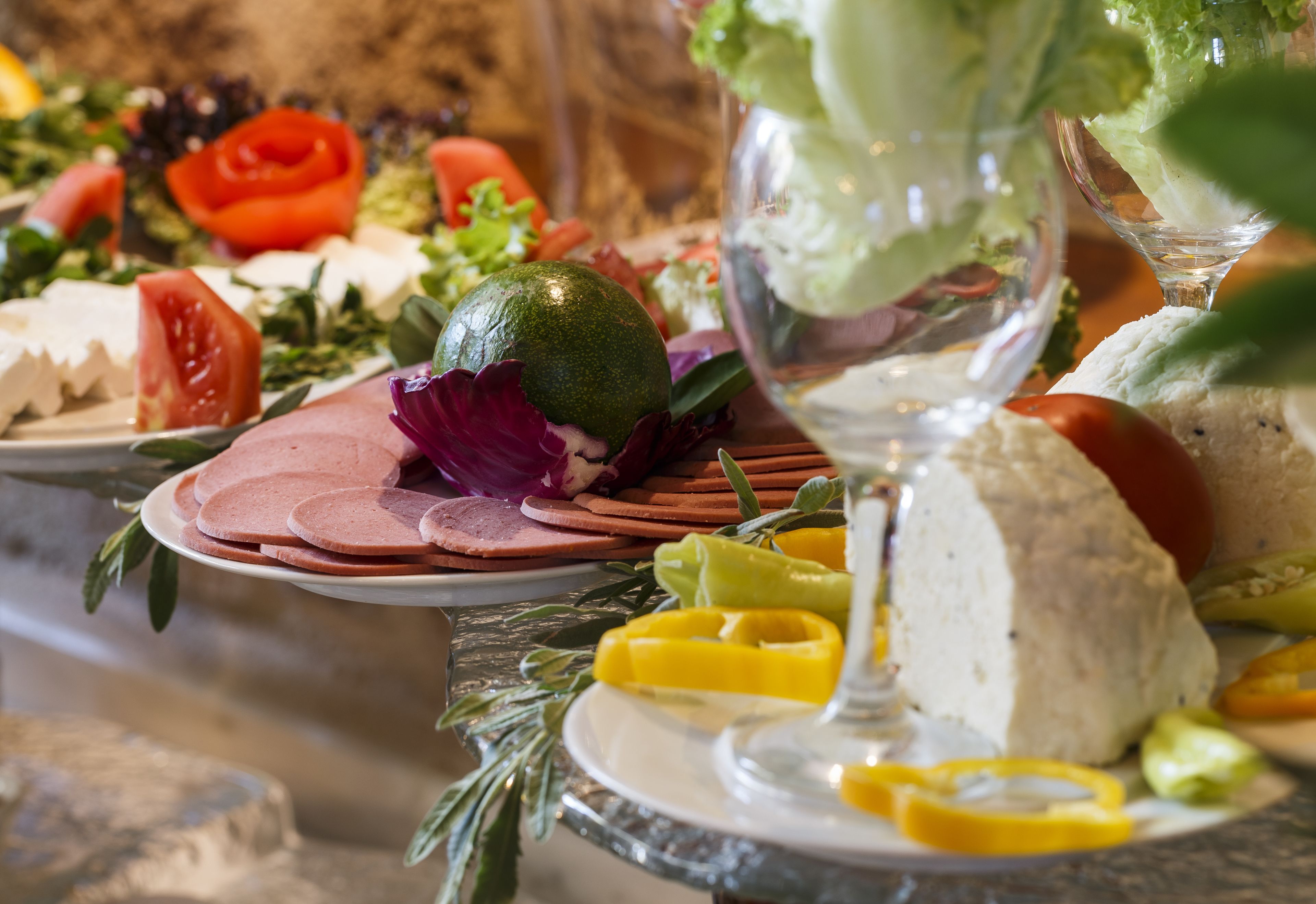 Variedad de quesos, frutas y verduras sobre una mesa, con una copa de vino blanco al frente.