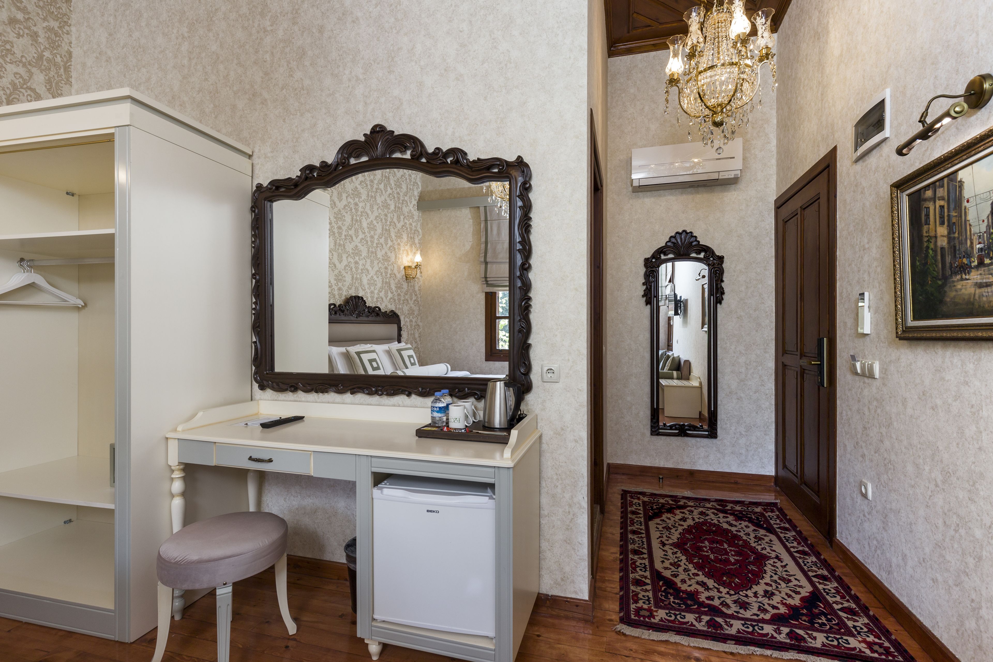 Une chambre à coucher de taille réduite, dotée d’une coiffeuse, d’un petit réfrigérateur, d’un fauteuil suspendu et d’un grand miroir.