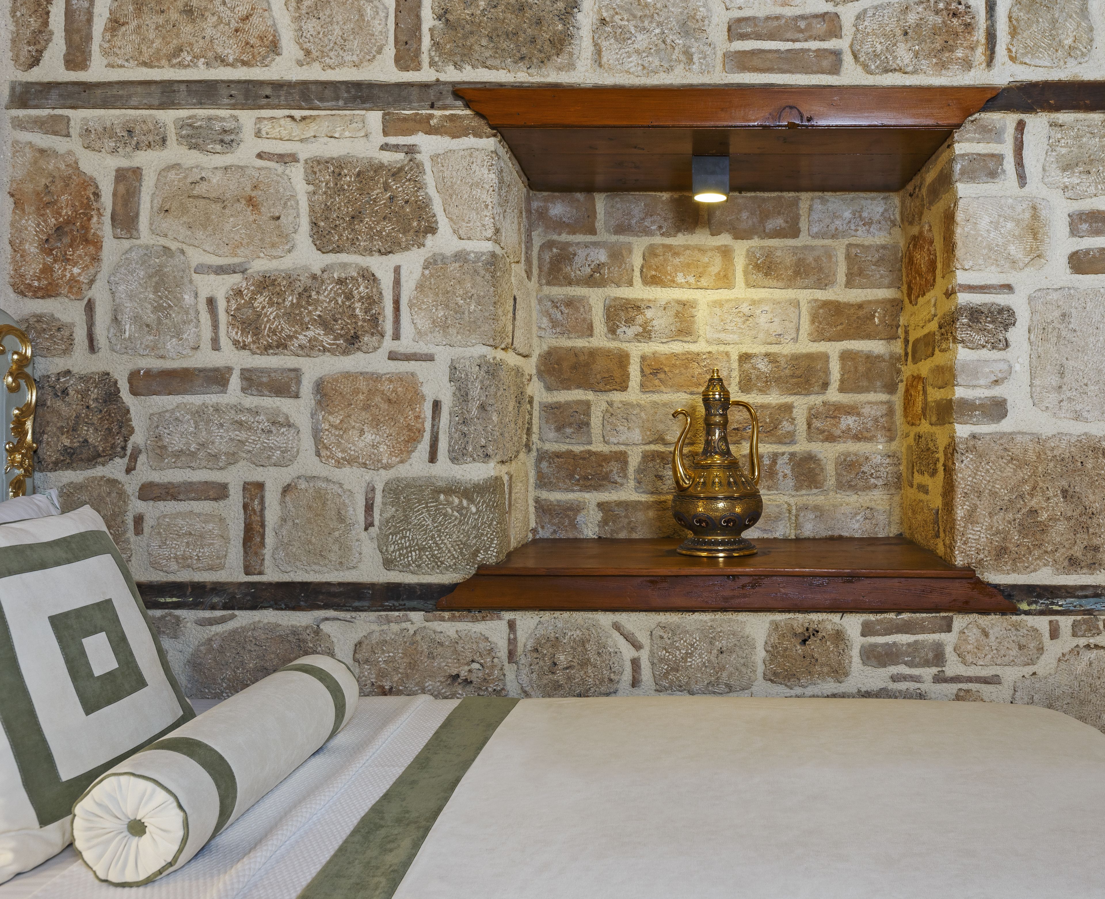 Un mur de pierre avec une étagère en bois et une lampe en laiton.