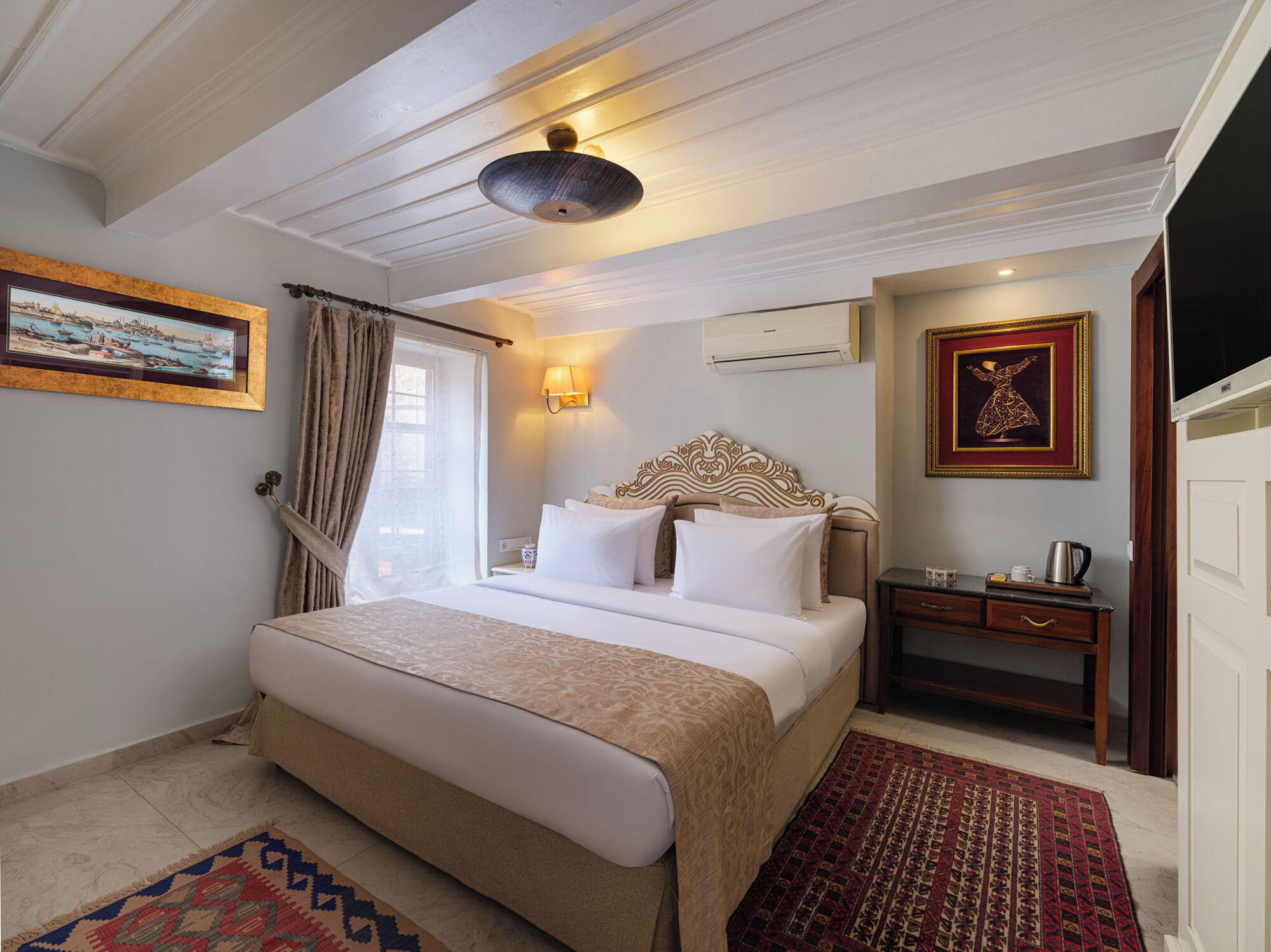 Une chambre d’hôtel avec un grand lit, une table de chevet, un appareil de climatisation, une télévision et un tableau encadré au mur.