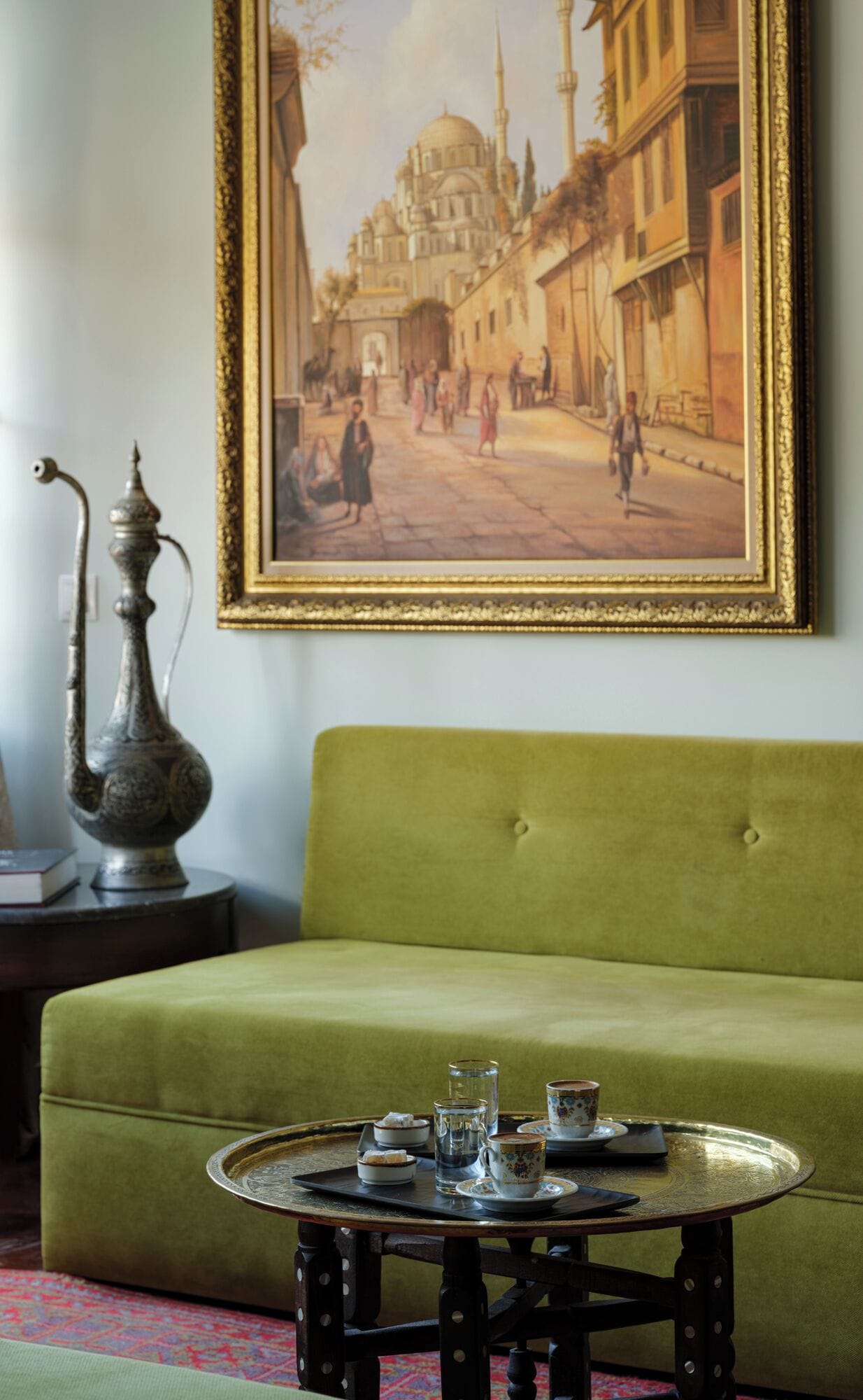 Habitación con sofá verde, una mesa con juego de té, bandeja de metal y un cuadro de un edificio histórico.