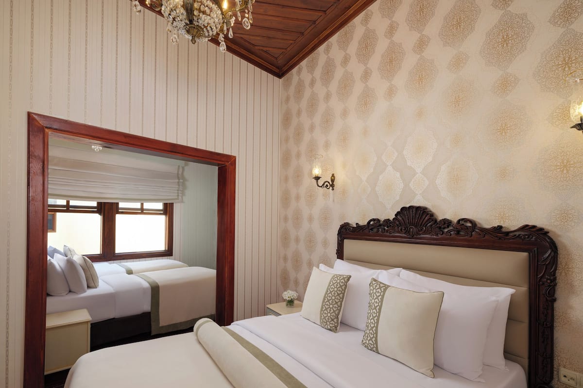 Een hotelkamer met een groot bed, een kleiner bed, een spiegel, een kroonluchter en behang met een patroon.