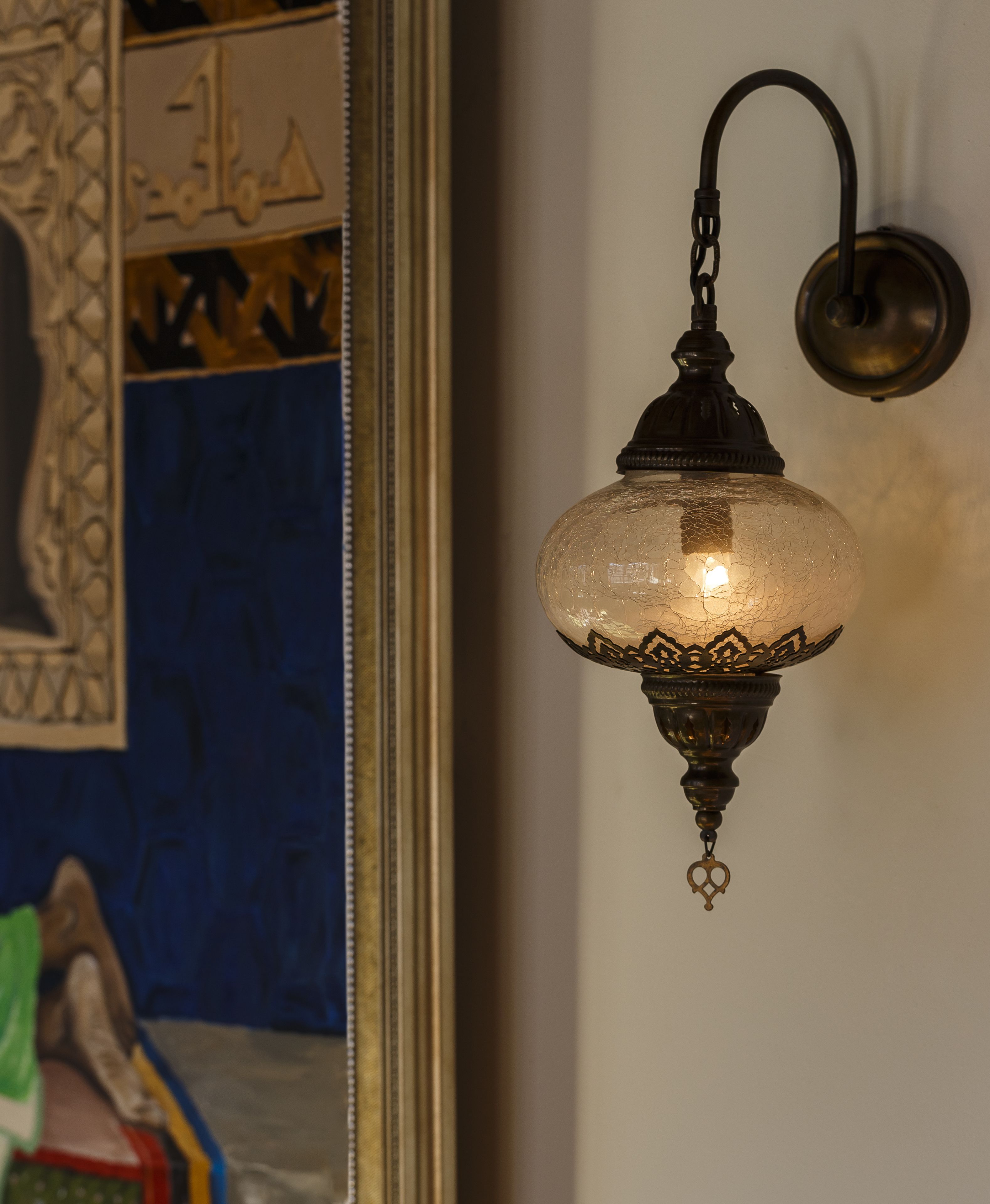 Een wandlamp met een decoratieve glazen kap en een metalen arm.