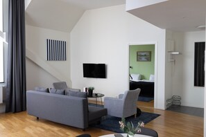 Un salon moderne avec un canapé gris, une petite table et un téléviseur à écran plat fixé au mur.