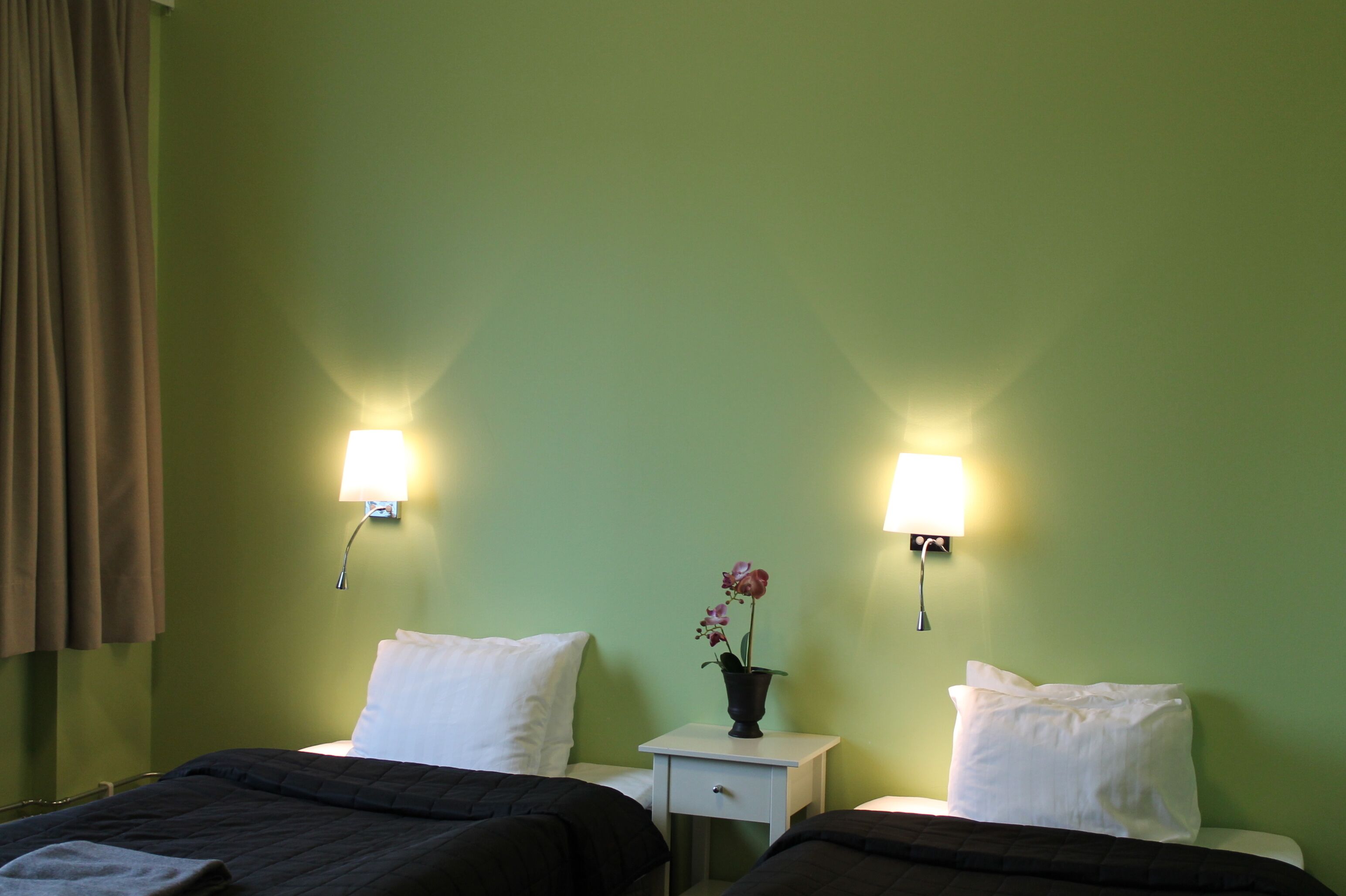 A hotel room with two beds, a nightstand with a lamp, and a vase with flowers.