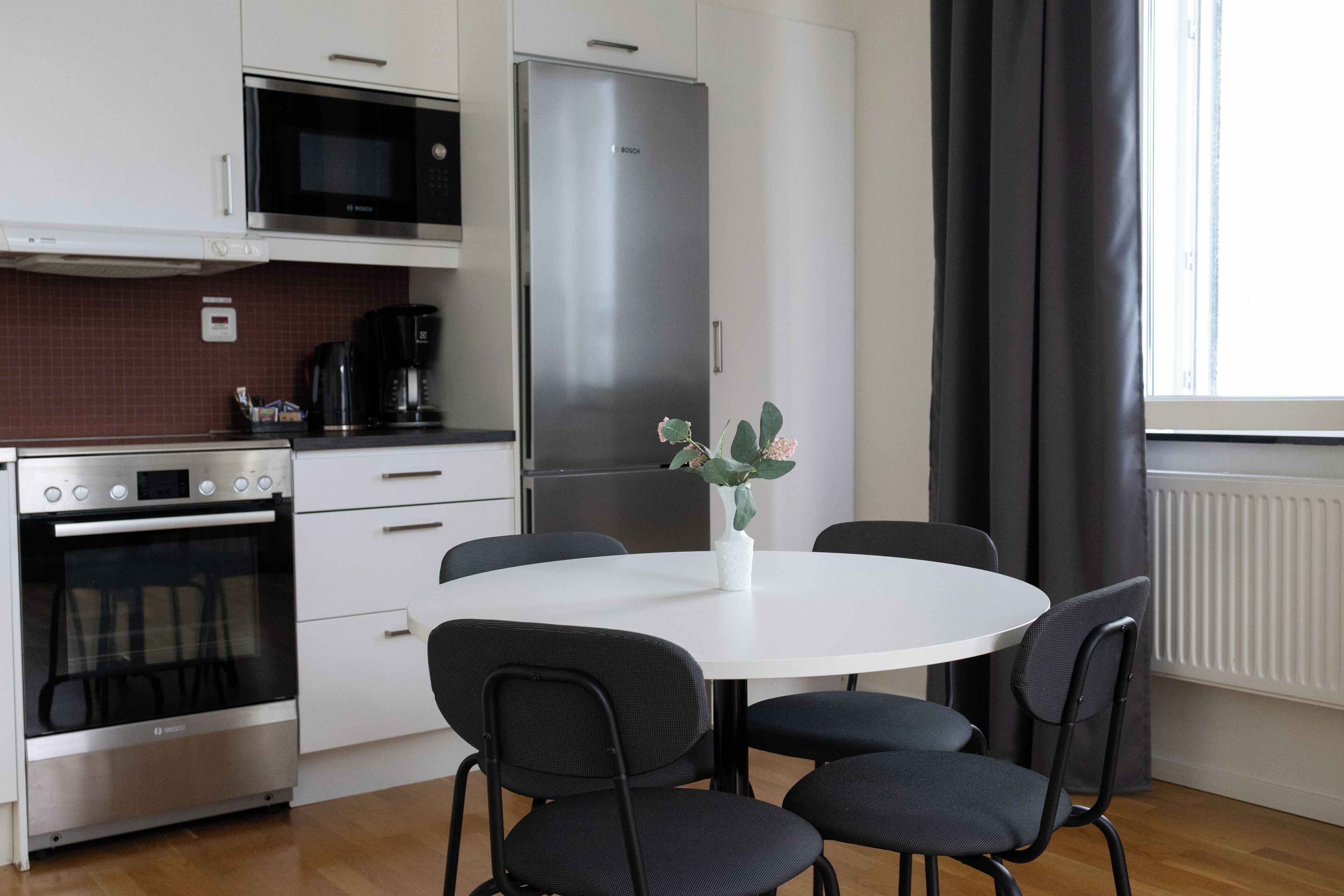 Et moderne køkken med mikroovn, komfur, køleskab og et spisebord med stole.
