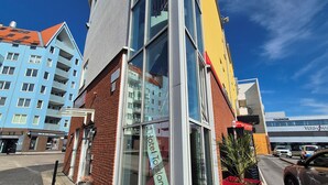 Un hôtel moderne avec une façade en verre, un jardinier rouge et un parking situé au premier plan.
