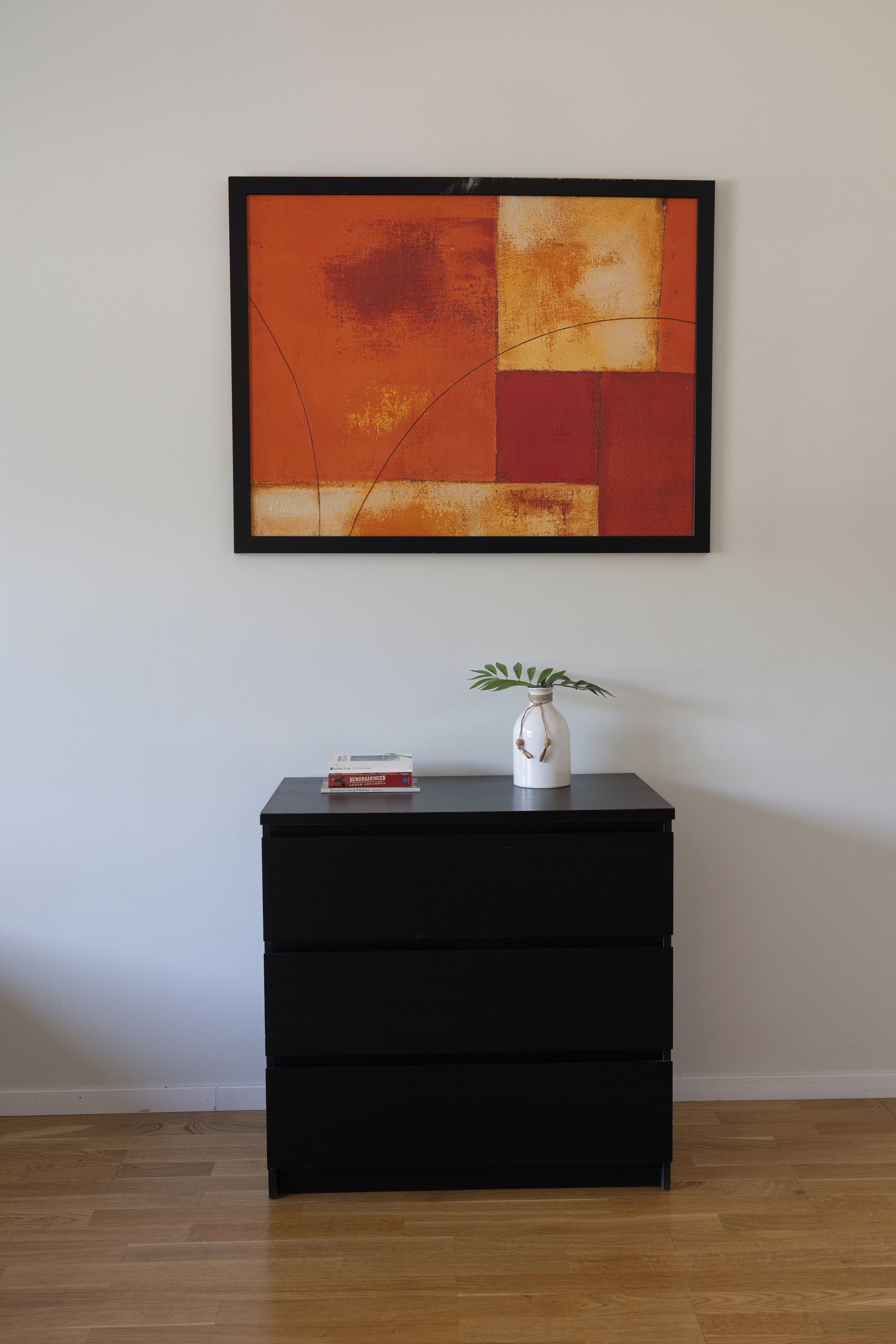 A black dresser with a white vase containing a plant and a book titled 'HUNDERAHRINGEN' on top.