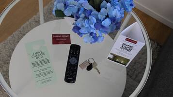 Ein Glastisch mit Fernbedienung, Schlüsseln, Parkausweis und einem QR-Code auf einer Hotelbroschüre.