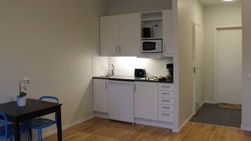 A compact kitchen with white cabinets, a microwave, and a sink. There is a small dining table with blue chairs and a potted plant.