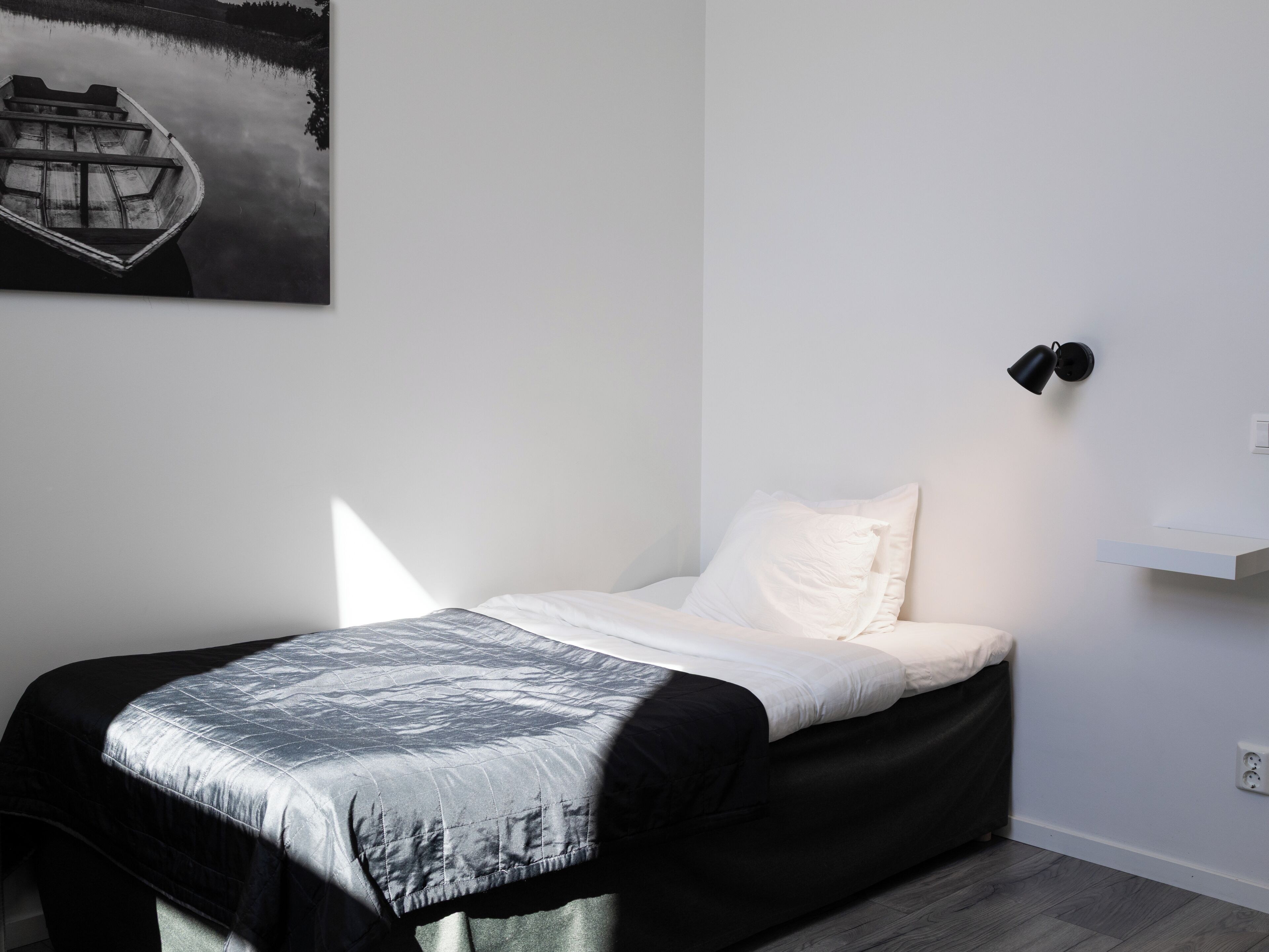 A bedroom with a bed, a nightstand, a wall-mounted lamp, and a painting of a boat on the wall.