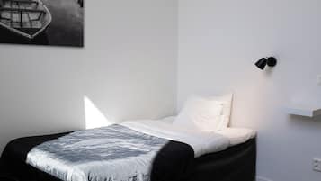 A bedroom with a bed, a nightstand, a wall-mounted lamp, and a painting of a boat on the wall.