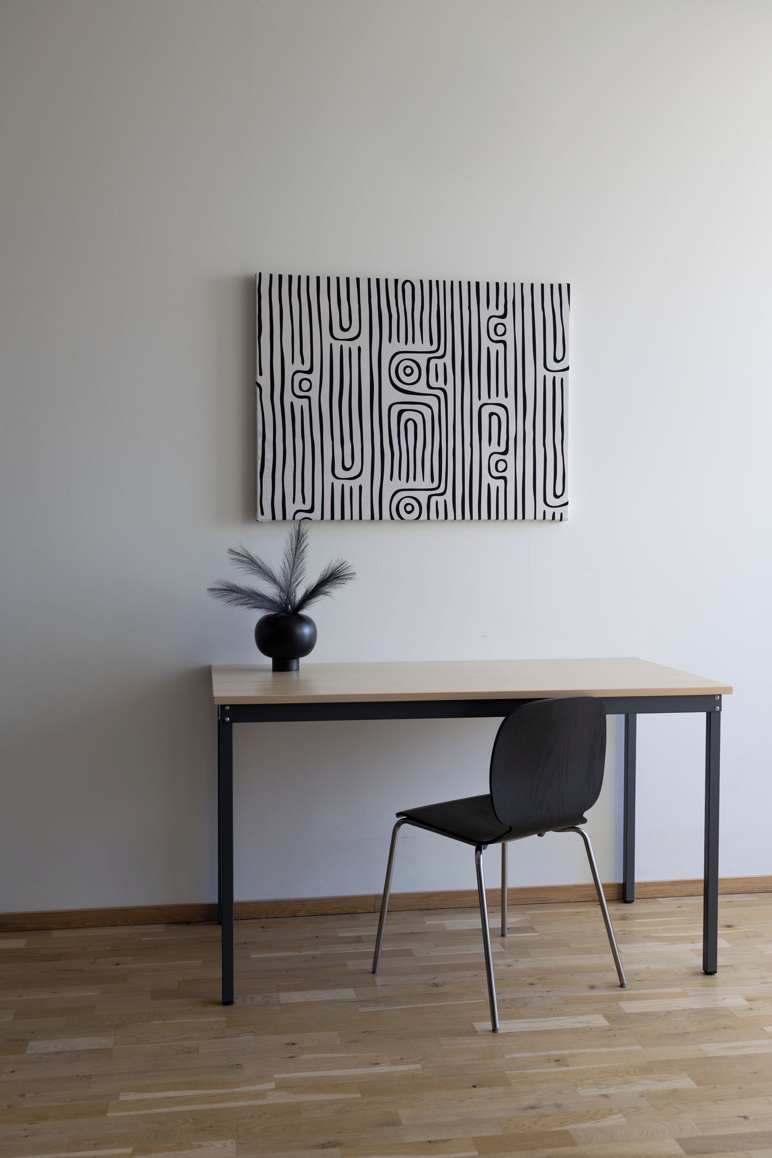A minimalist room with a wooden desk, a black chair, and a wall-mounted abstract art piece.
