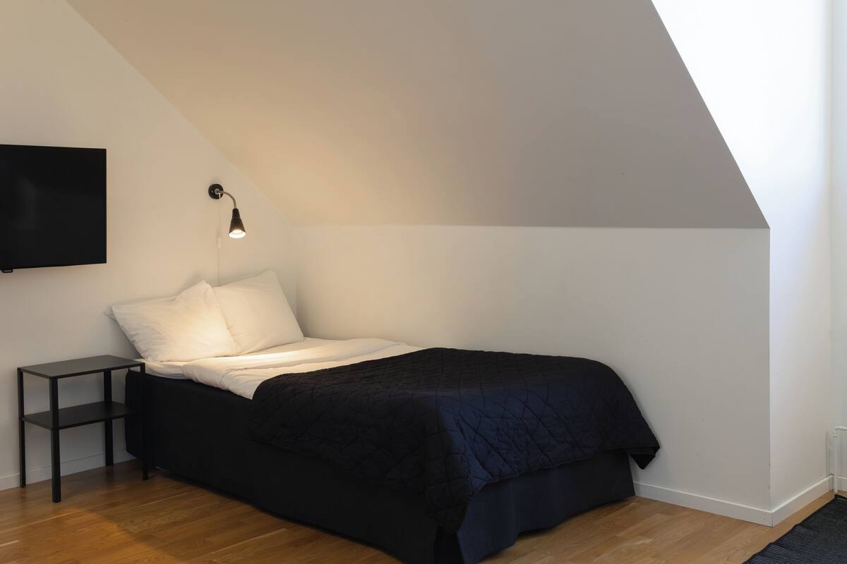Ein Schlafzimmer mit einem Bett, einem Nachttisch, einer Lampe und einem an der Wand befestigten Fernseher.