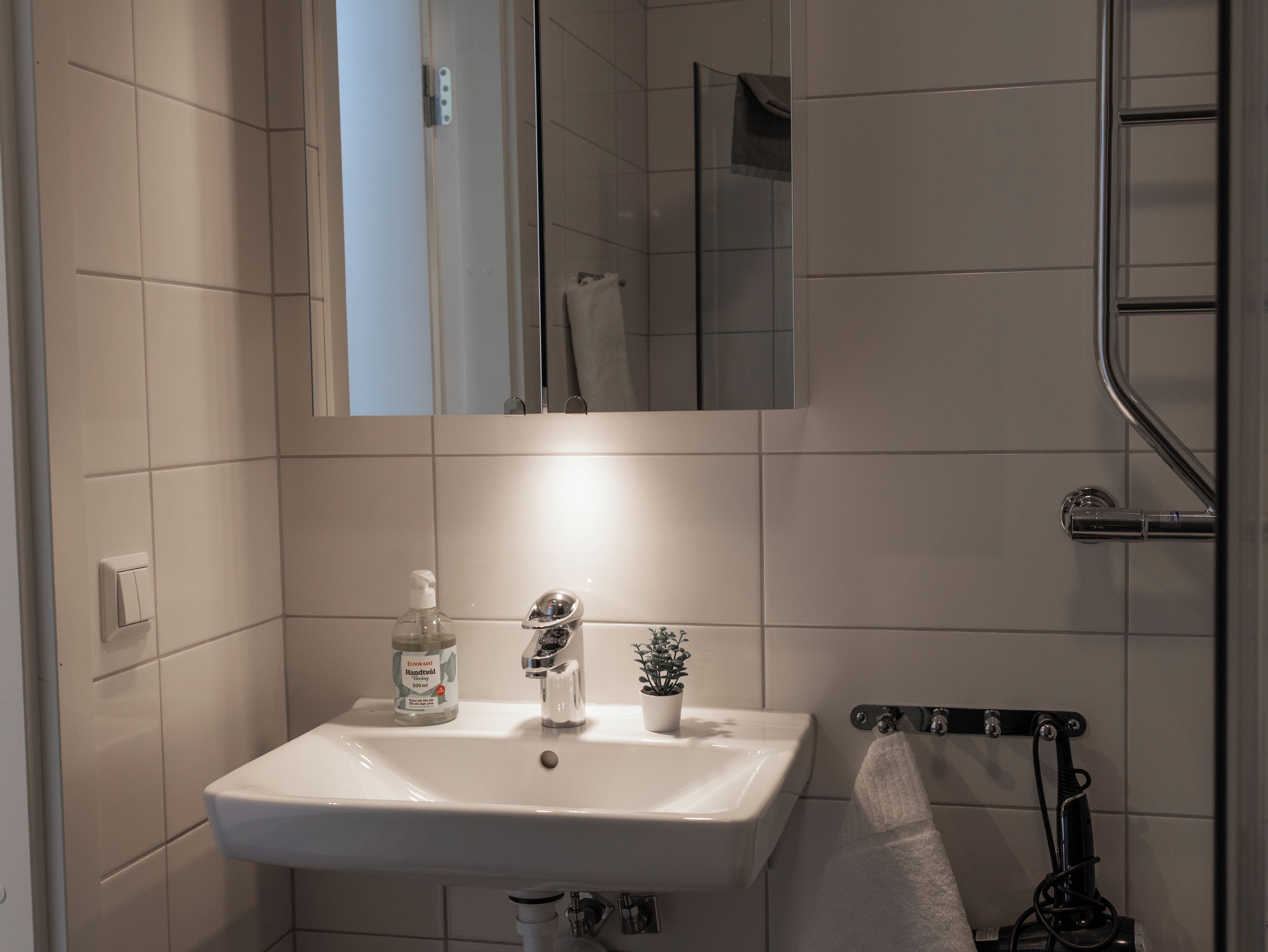 Une salle de bain avec un lavabo blanc, un miroir, un porte-serviettes et un espace douche.