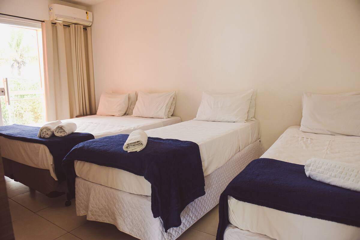 Ein Hotelzimmer mit drei Betten, jeweils mit einer weißen gesteppten Matratze und einer dunkelblauen Decke.