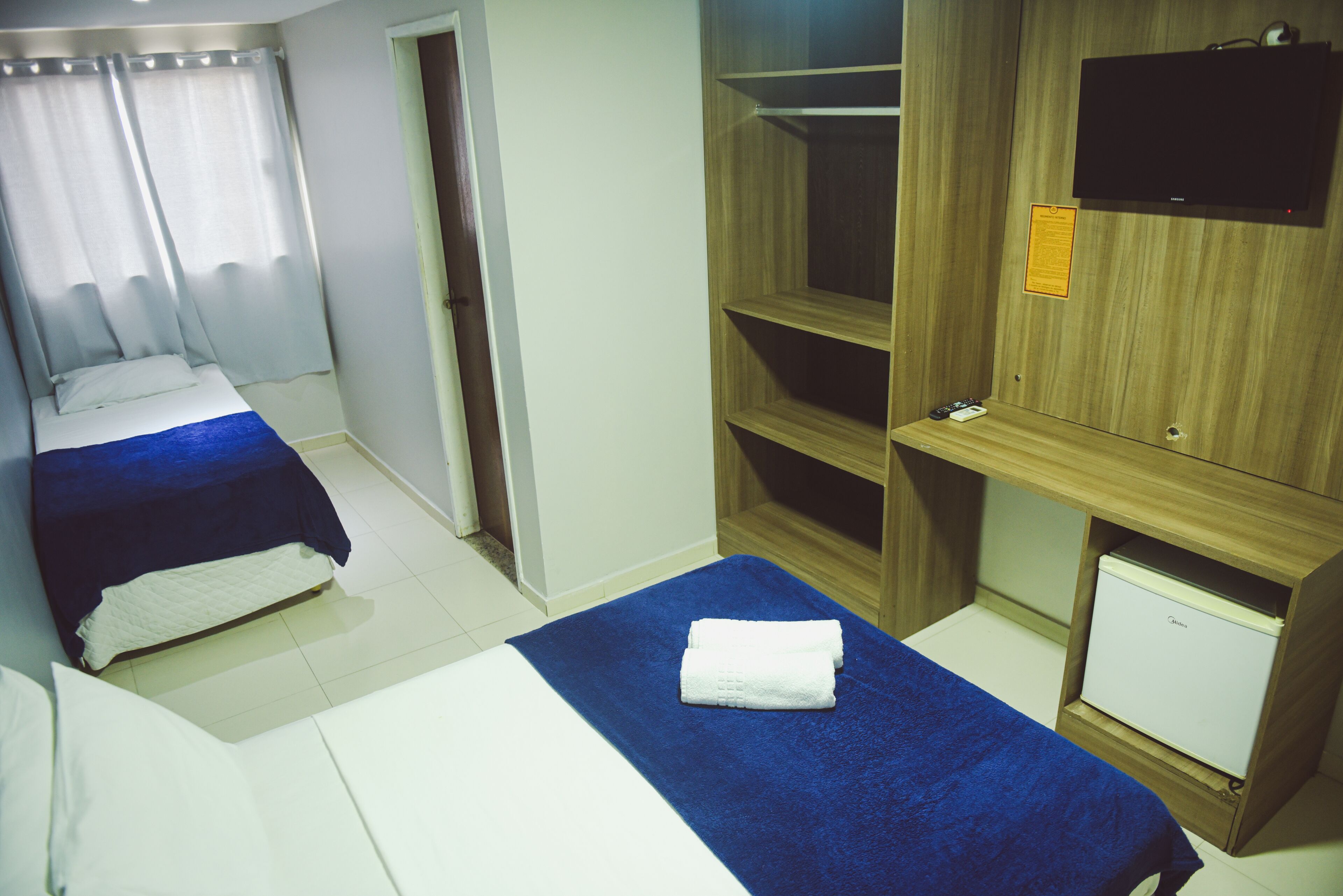 A hotel room with two beds, a small TV, a wardrobe, and a desk.