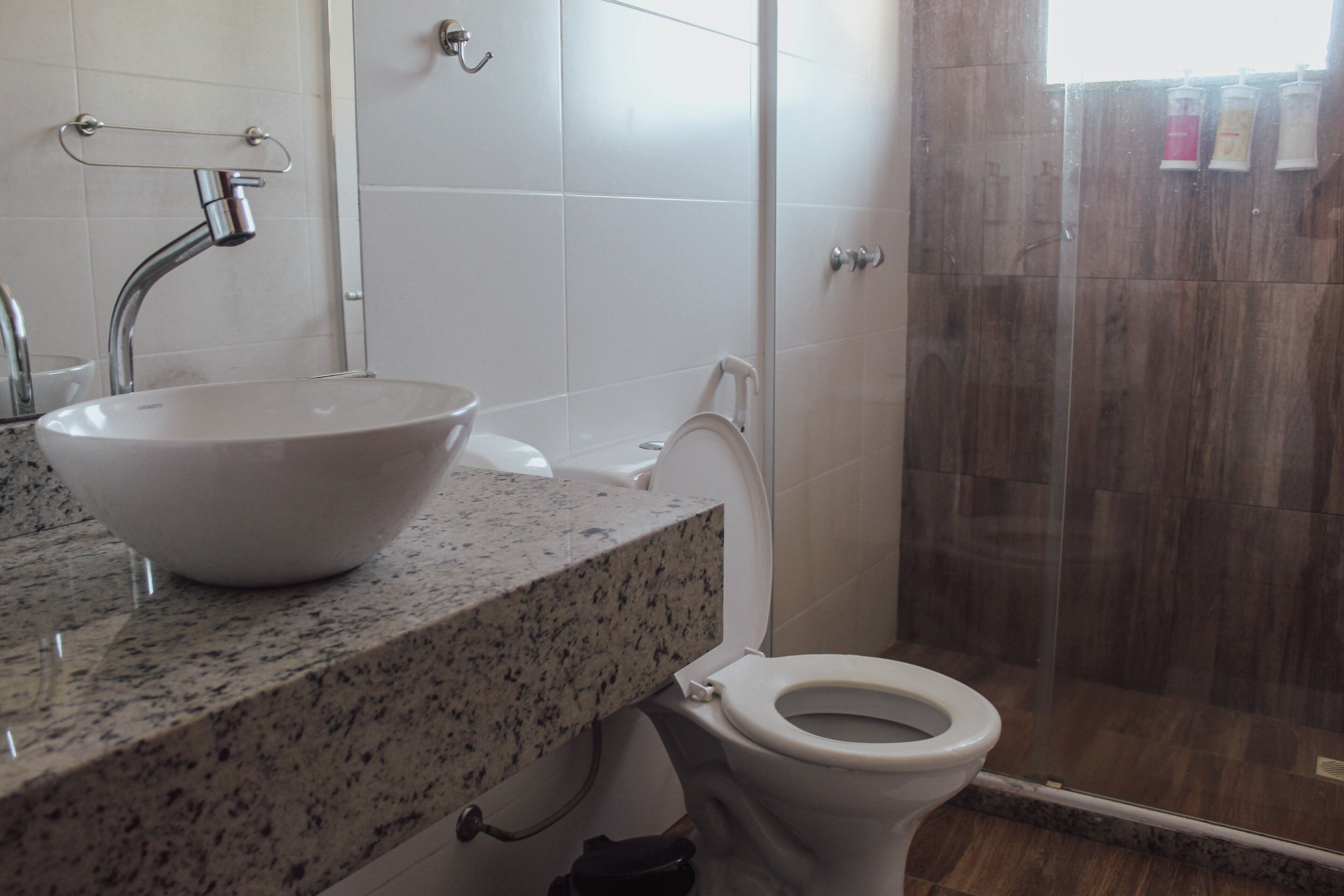 A bathroom with a granite countertop, a white sink, a toilet, and a glass shower enclosure.