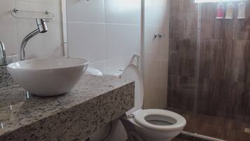 A bathroom with a granite countertop, a white sink, a toilet, and a glass shower enclosure.