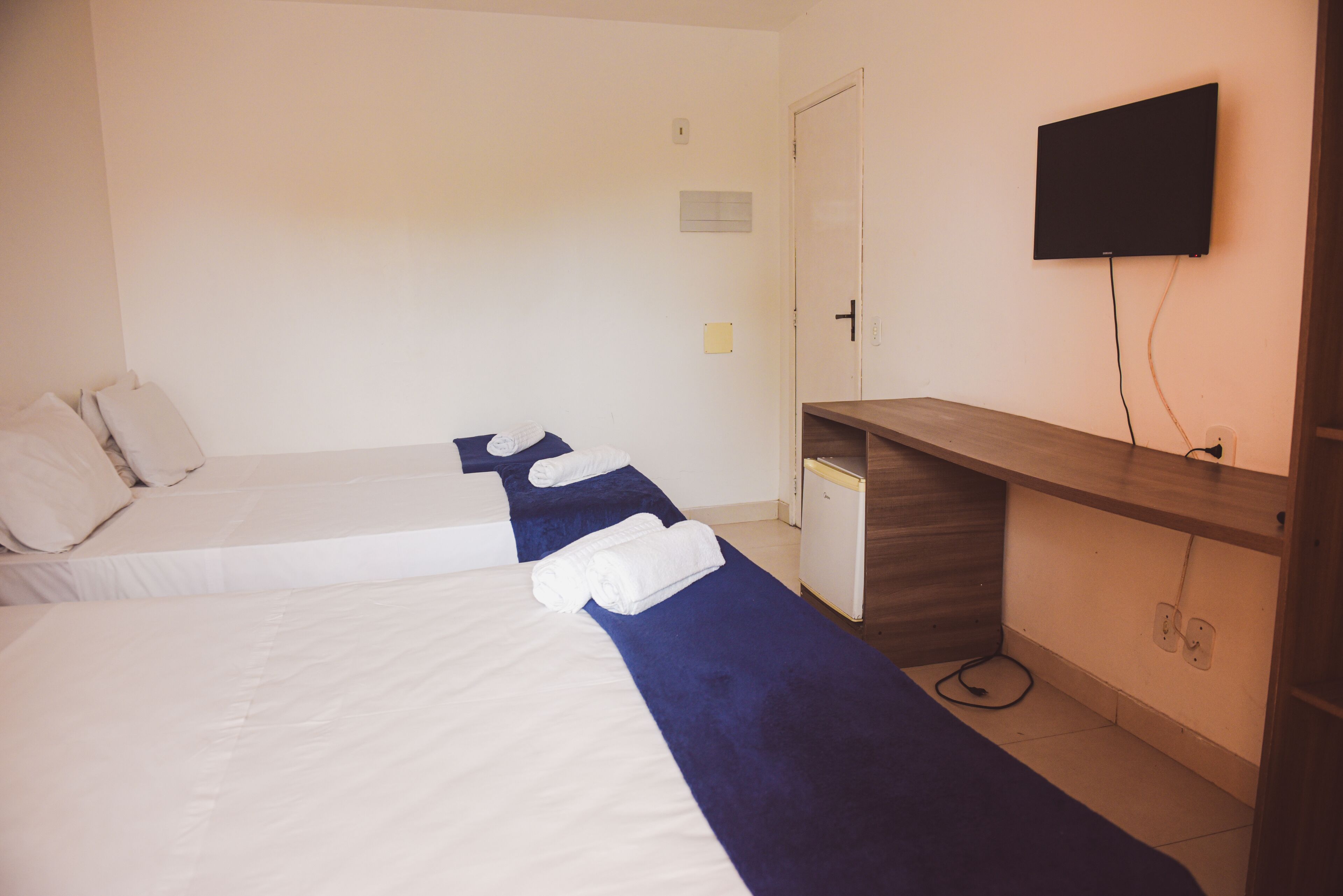A hotel room with two beds, a TV mounted on the wall, and a wooden desk.