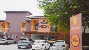 A building with a sign reading "Xerxes Pousada" and a parking lot with several cars. - Pousada Xerxes (Arraial do Cabo)