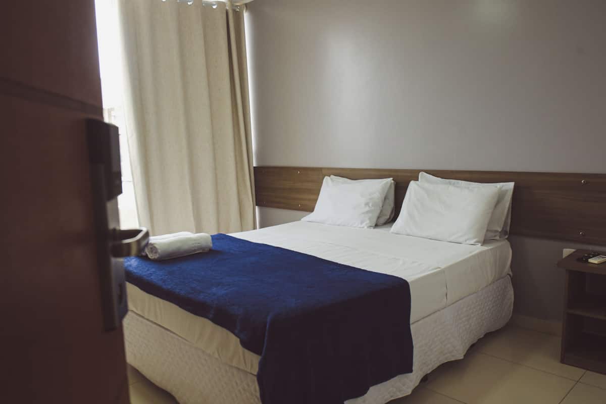 Ein Hotelzimmer mit einem Bett, einem Holzkopfbrett, einem Nachttisch und einem Fenster mit Vorhängen.