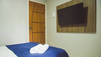 Quarto de hotel com cama, porta de madeira, TV de tela plana na parede e toalha sobre a cama.