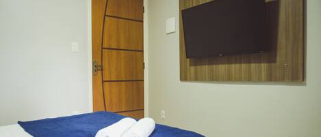 A hotel room with a bed, a wooden door, a flat-screen TV mounted on the wall, and a towel on the bed.