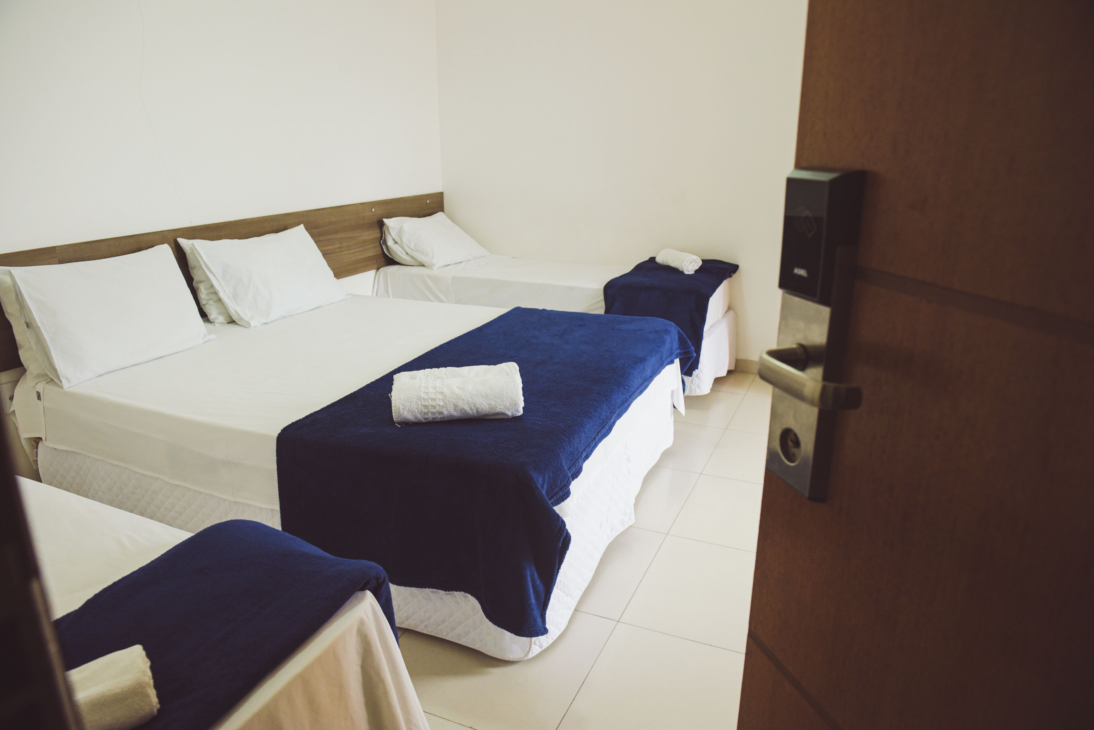 A hotel room with three beds, each with a blue blanket and white pillows.