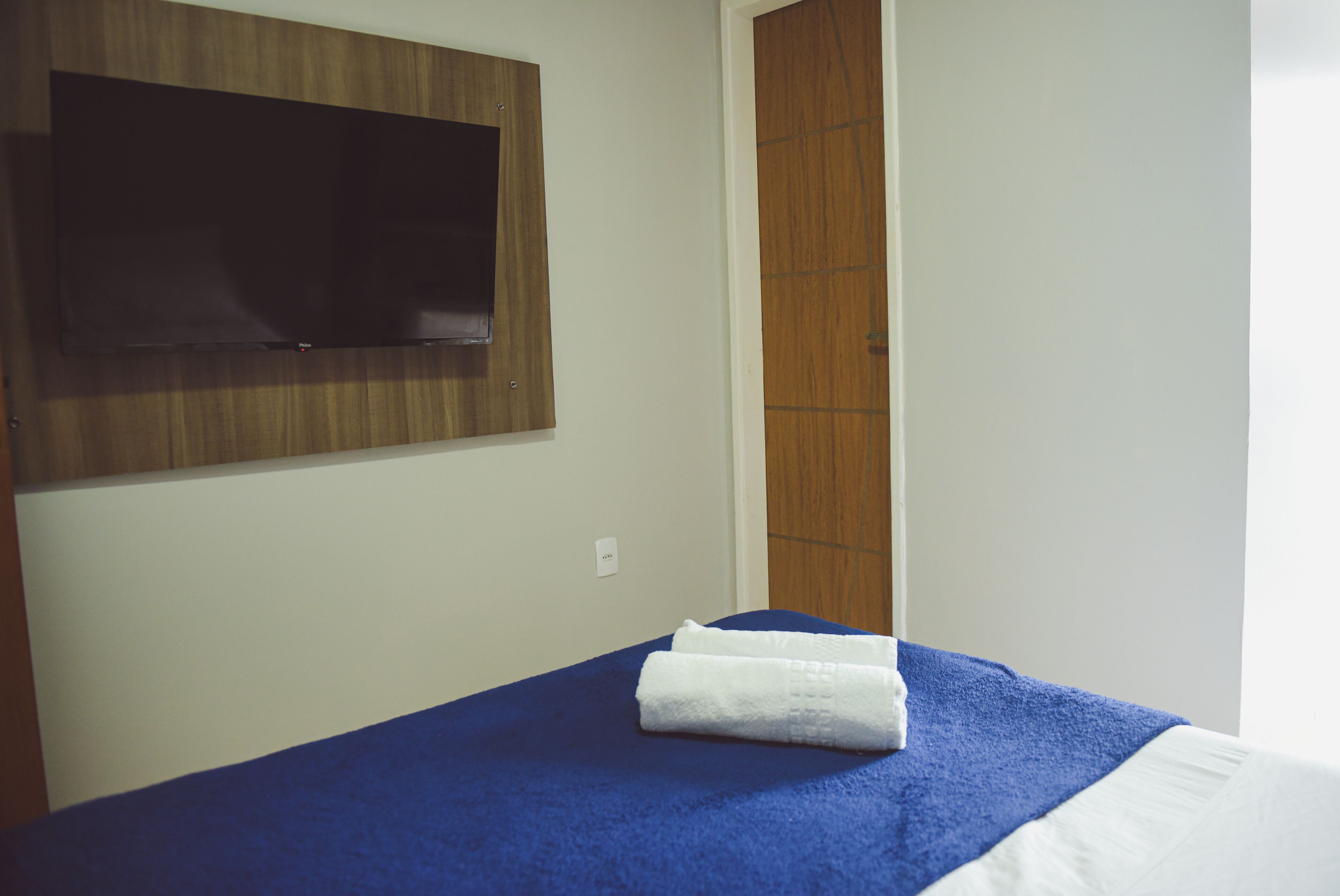 A hotel room with a bed, a flat-screen TV mounted on the wall, and a wooden door.